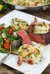 Grilled steak tenderloin topped with shrimp scampi and served with a garden salad. Steak is cut to show a close-up of the rosy pink center, cooked to medium-rare.