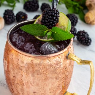 Ginger-Blackberry Cocktail in a copper mug garnished with blackberries, mint and lime.
