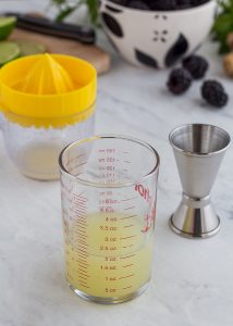 measuring cup and juicer cup with lime juice on a marble table