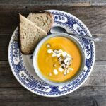 Butternut soup in a bowl on a blue and white plate with dipping bread.