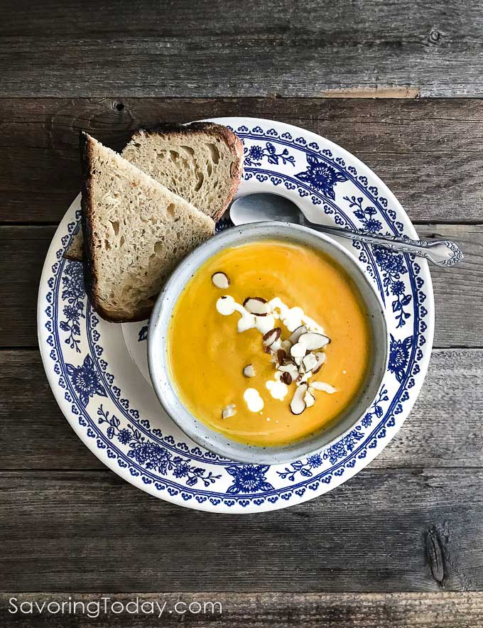 Butternut soup in a bowl on a blue and white plate with dipping bread.