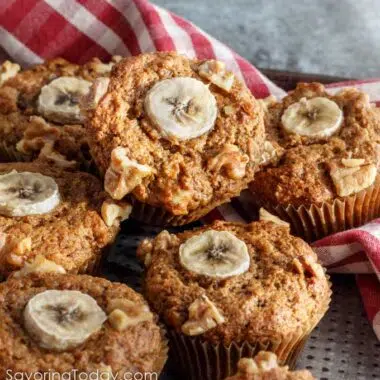 Sprouted wheat muffins with banana and walnut garnish stacked on a pan.