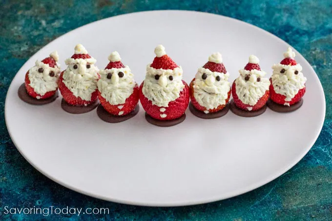 Cheesecake stuffed strawberries decorated to look like Santas on a white platter.