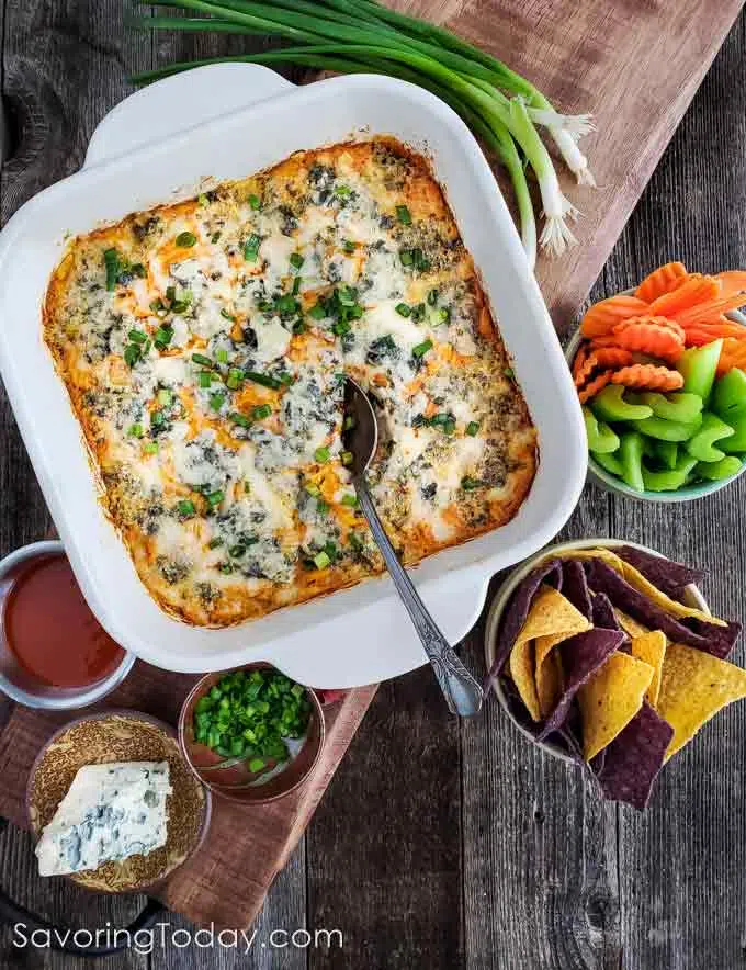 Buffalo Chicken Dip in a white casserole dish with carrots, celery and chips on the side.