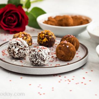 Chocolate truffles on a white place with bowls of coatings beside it.