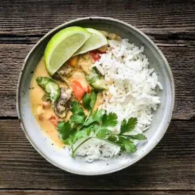 Vegetable coconut curry in a grey bowl with jasmine rice topped with lime and cilantro.