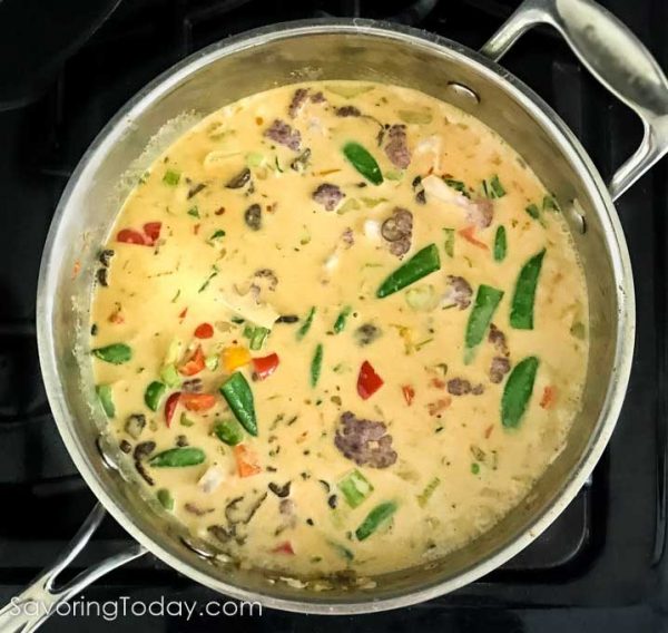 Vegetables in yellow curry sauce in a stainless steel pan.