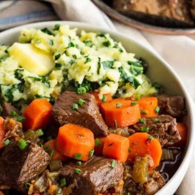Irish beef stew and carrots with mashed sweet potatoes and kale in a beige bowl.
