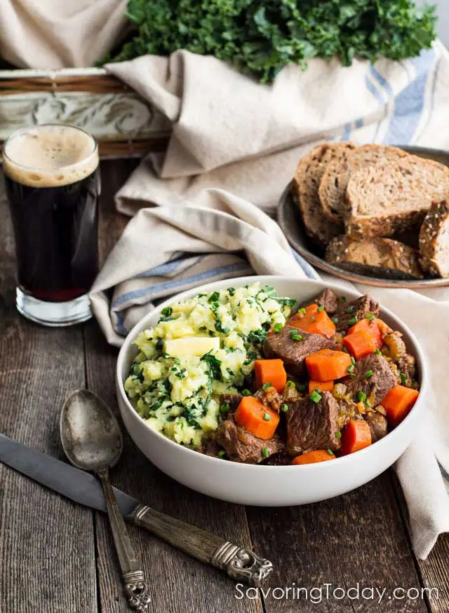 Guinness Beef Stew in a white bowl on a table with a dark beer and bowl of bread.