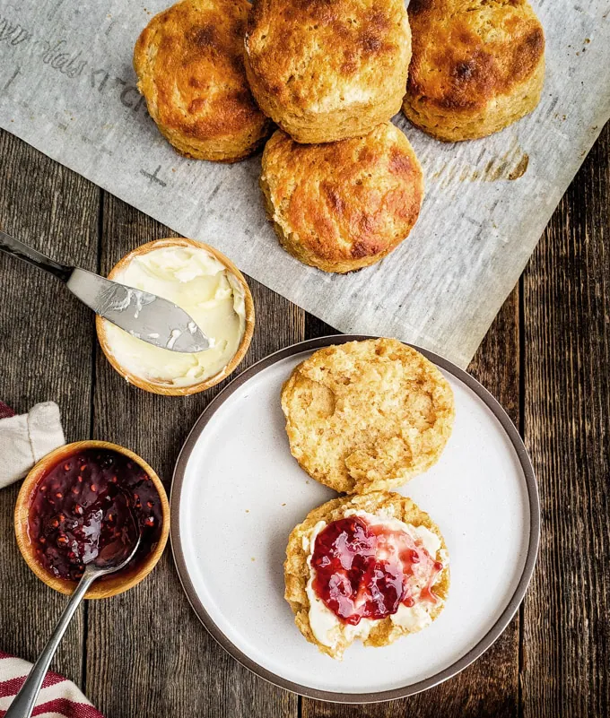 Biscuit open on a plate with butter and raspberry jam on half.