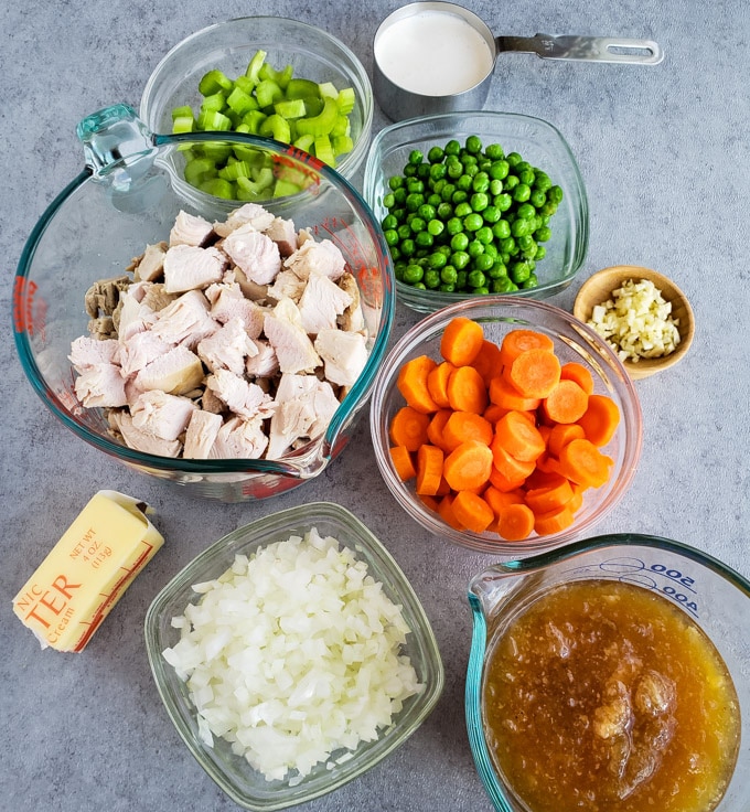 Cubed turkey, sliced carrots, chopped celery, peas, onions, and stock all in separate dishes for making Turkey Pot Pie.