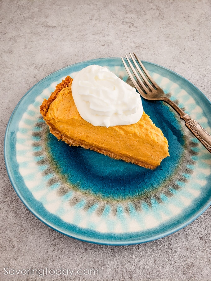 A slice of pumpkin dream pie with whipped cream on top served on a blue plate.