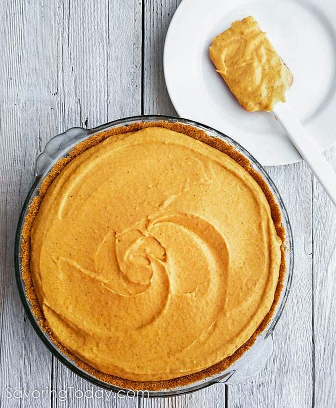 Pumpkin dream pie made from scratch in a pie dish on a white wood table.