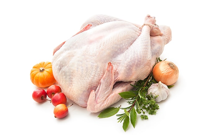 Uncooked turkey on a white background with fruit and vegetables around it.