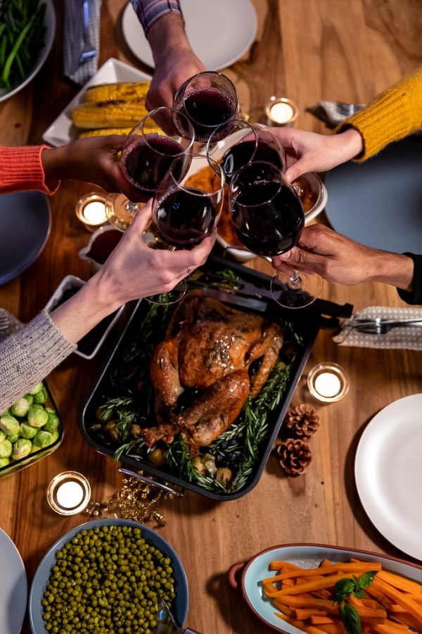 Overhead view of the hands of a group of young adult friends sitting at a table at home set for Thanksgiving