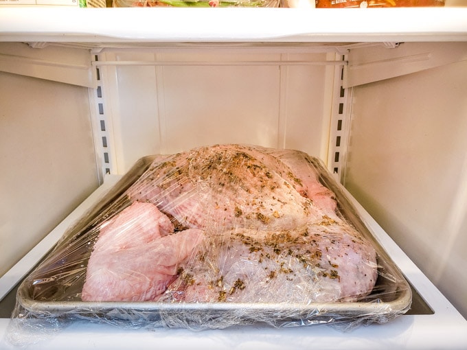 Turkey covered with plastic wrap to rest in the fridge.