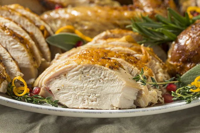 Roasted turkey sliced and served on platter with herbs and lemon peel.