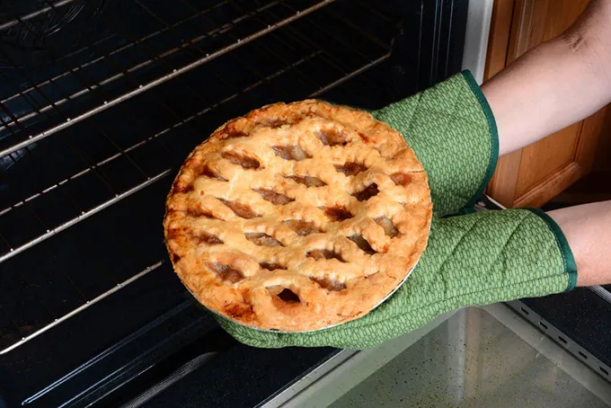 Hands with oven mitts taking pie from the oven