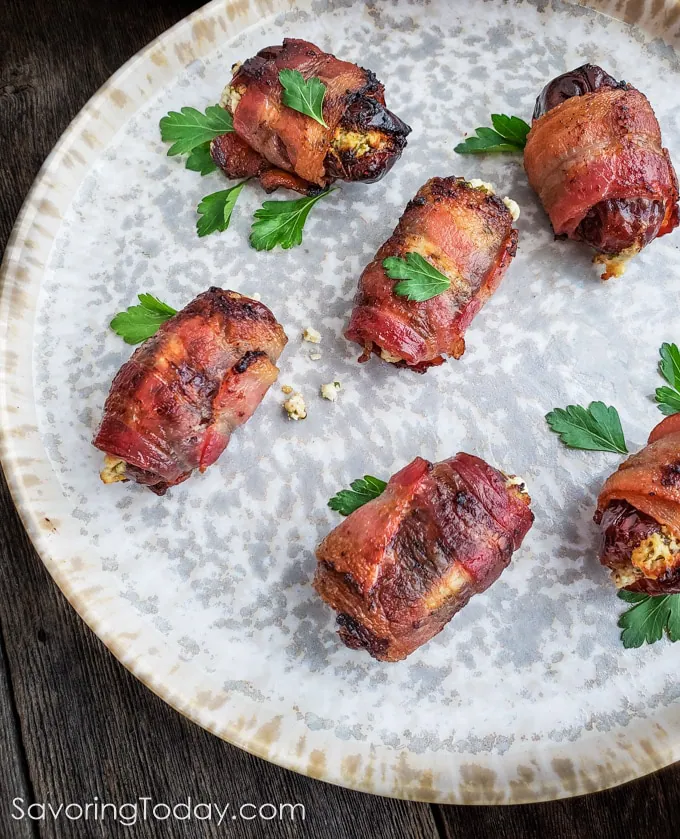 Bacon wrapped around dates filled with goat cheese on a plate with parsley leaves scattered around it.