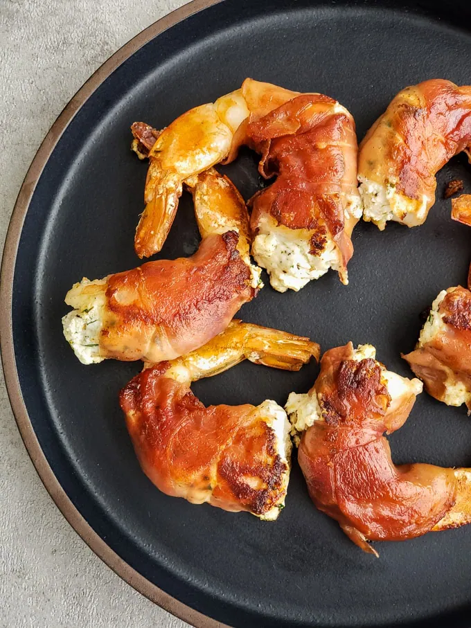 Close up of prosciutto wrapped shrimp with goat cheese on a dark plate.