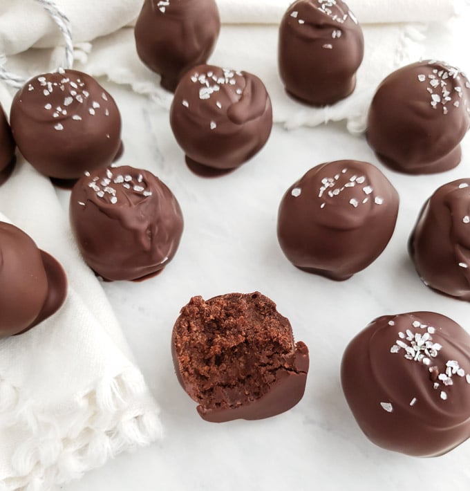 Chocolate truffles with a sprinkle of sea salt on a marble board and one with a bite out of it. 