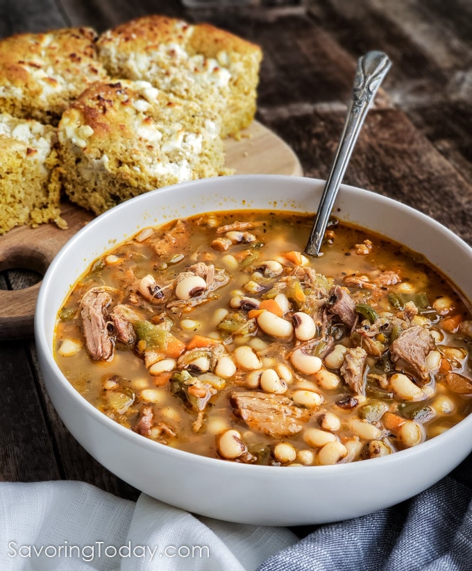 Black eyed pea soup with pulled pork and green chiles in a white bowl beside cornbread.