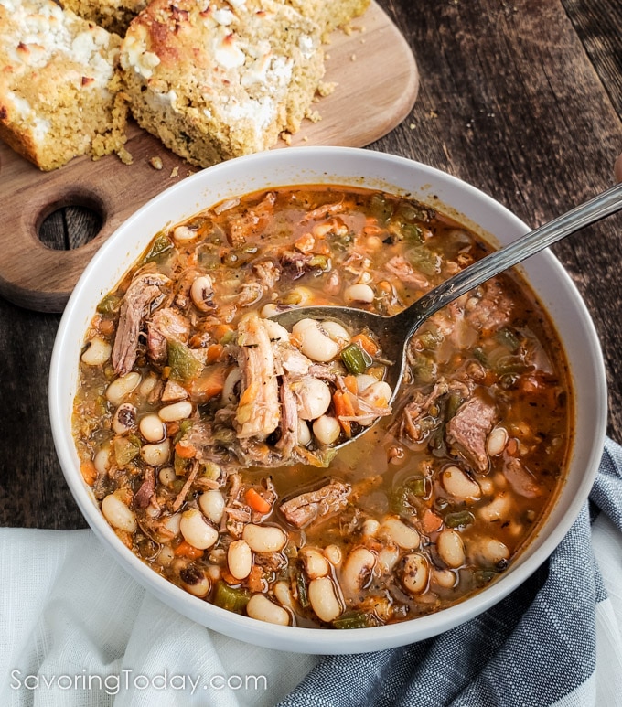 Black-eyed pea soup with pulled pork and green chiles scooped up in a spoon over the bowl.