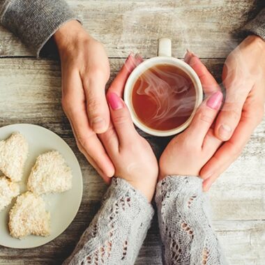 Couple's hands around a cup of tea with heart shaped cookies