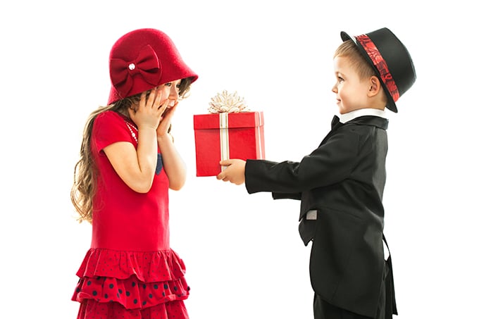 kids dressed up with boy giving gift to surprised girl