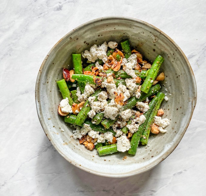 Green beans tossed with brown butter, hazelnuts, and goat cheese in an earthenware bowl.