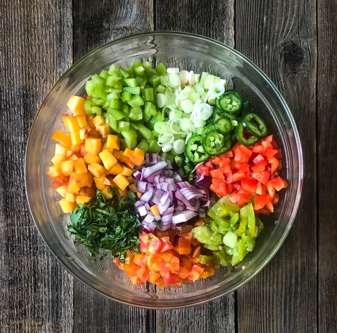 Diced peaches, tomatoes, bell pepper, jalapeno, green and red onion, and cilantro in a bowl for salsa.