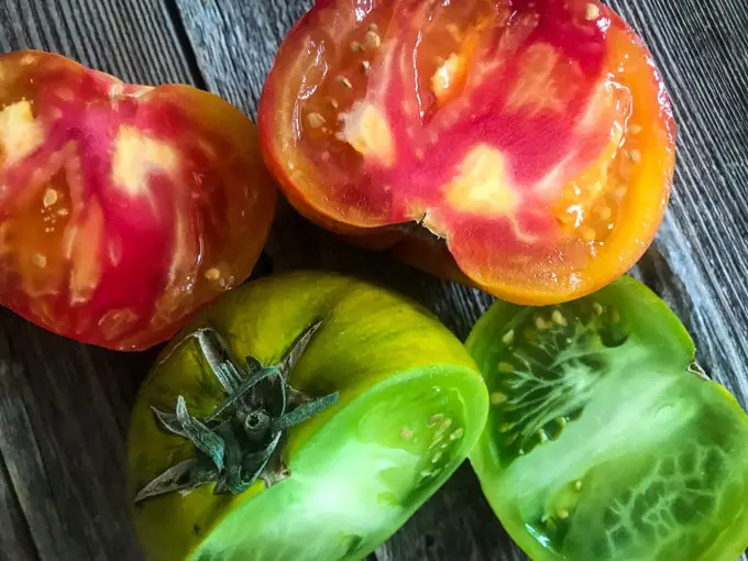 Beefsteak and Cherokee Green Heirloom tomatoes cut in two on a wood board.