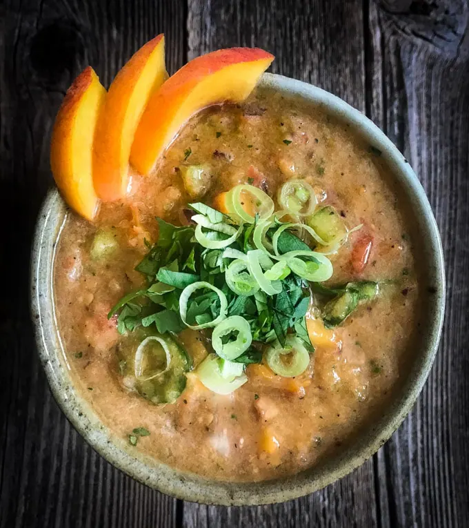 Peach and tomato salsa with sliced green onion and cilantro garnish in a bowl on a wood table.