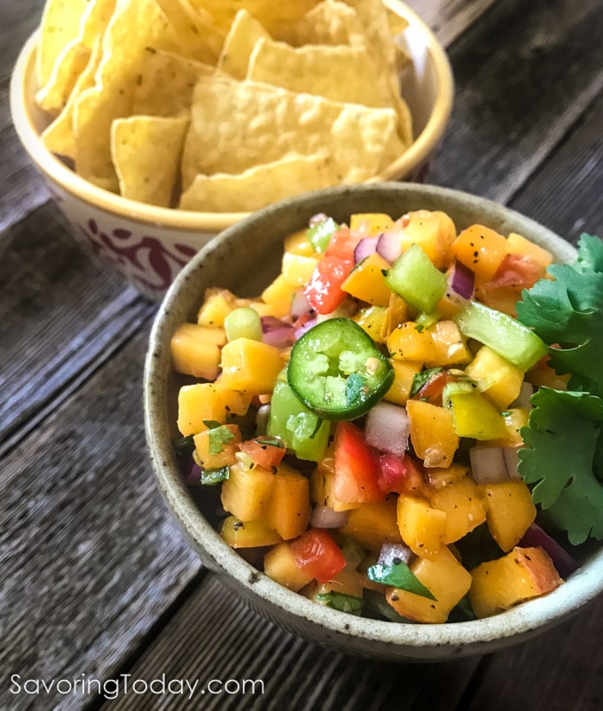 Chunky peach and tomato salsa in a bowl with a jalapeno on top.
