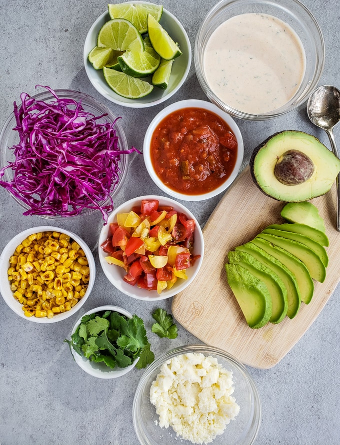 Cabbage, lime, salsa, tomatoes, avocado, corn, cilantro, and cotija cheese in separate bowls for topping tacos