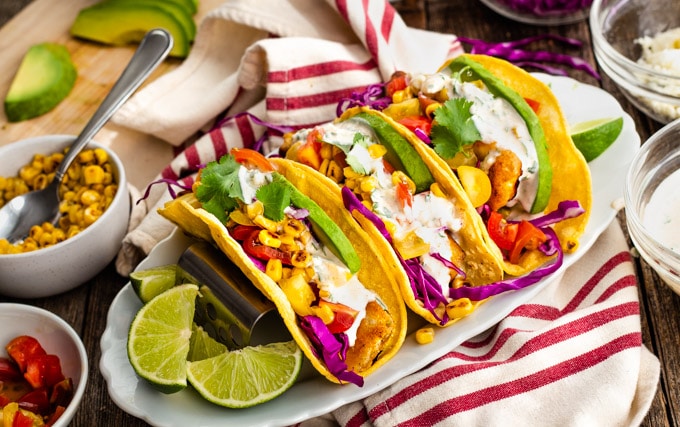 Three fish tacos in corn tortillas on a striped towel with limes.