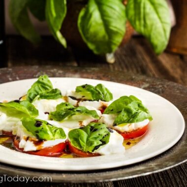 Sliced tomatoes and buffalo mozzarella on a plate topped with basil.