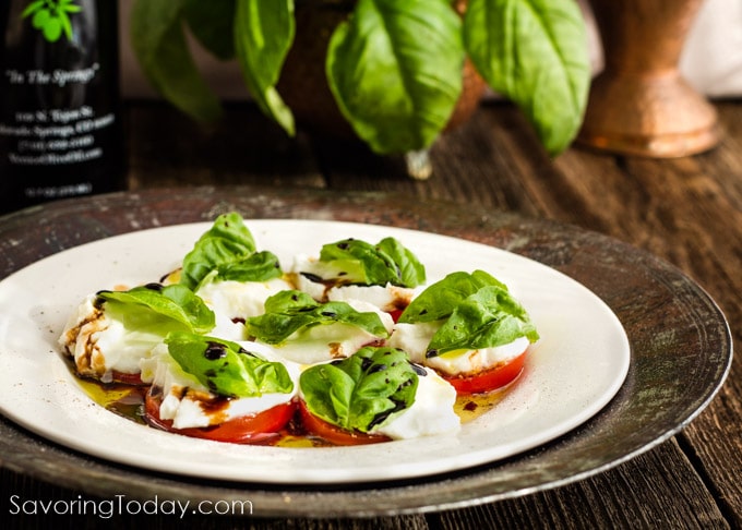 Sliced tomatoes with buffalo mozzarella on top with a basil leaf on a white plate.