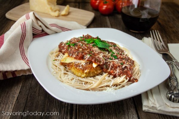 Chicken parmesan with marinara over pasta on a white plate on a table.