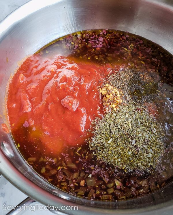 Tomatoes, herbs, and seasoning resting on top of marinara sauce in a stainless steel pan.