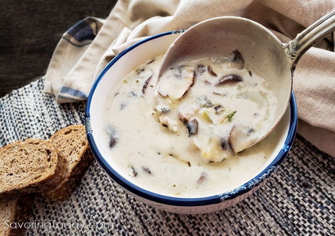 Small bowl of creamy mushroom soup with a ladle in it on a table with bread.