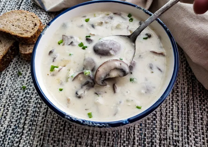 A spoon lifting a bite of mushrooms  out of a bowl.
