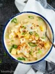 Bowl full of creamy cauliflower, potato, leek soup with a spoon ready to serve up a bite.