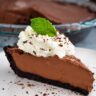 A slice of mint chocolate cream with with a dollop of fresh whipped cream, a sprinkle of cocoa, and a mint leaf