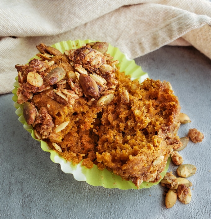 A pumpkin muffin with crumb topping broken open on a counter to show the moist crumb.