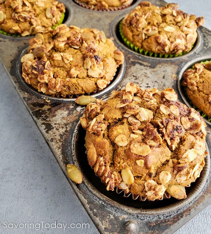 Muffin made with pumpkin topped with oats and pepitas in a muffin tin.