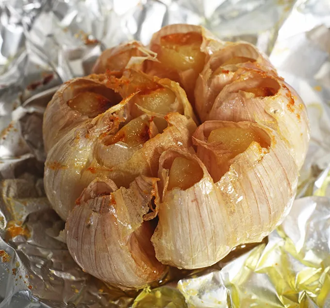 A head, or bulb, of freshly roasted garlic, still on the tinfoil it was cooked in after having the top chopped off and oil poured on.