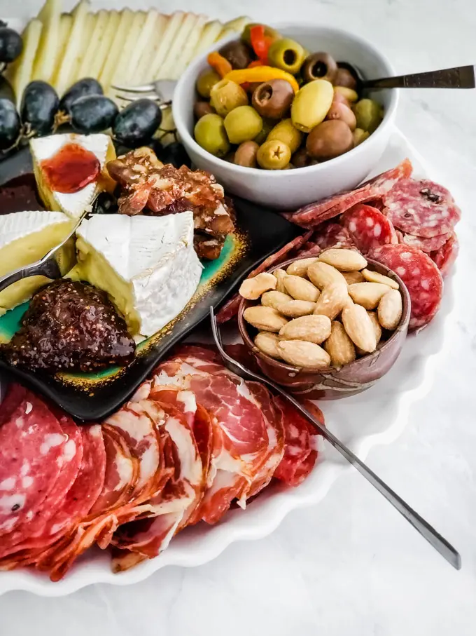 a charcuterie tray with sliced meat, marcona almonds, assorted olives, and cheese