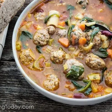 Minestrone soup with Meatballs in a white bowl with a spoonful