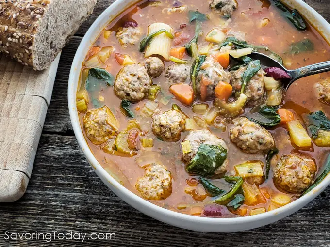 Minestrone soup with Meatballs in a white bowl with a spoonful